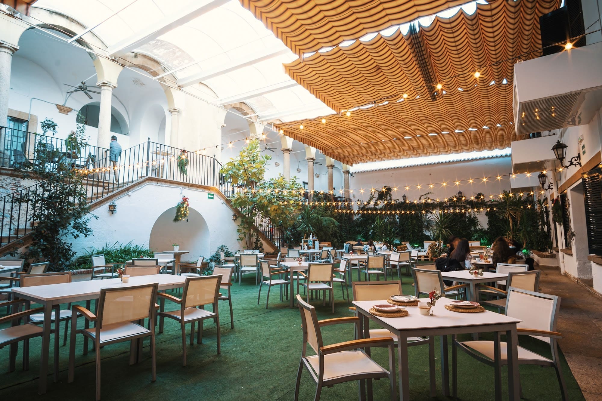 El patio de día, con el toldo de cañizo, los muros encalados y las mesas puestas